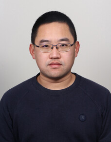 Herr Huang mit Brille und schwarzem Shirt, neutraler Ausdruck.